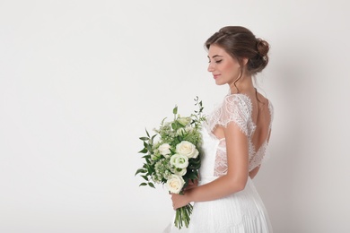 Photo of Young bride wearing wedding dress with beautiful bouquet on light background. Space for text