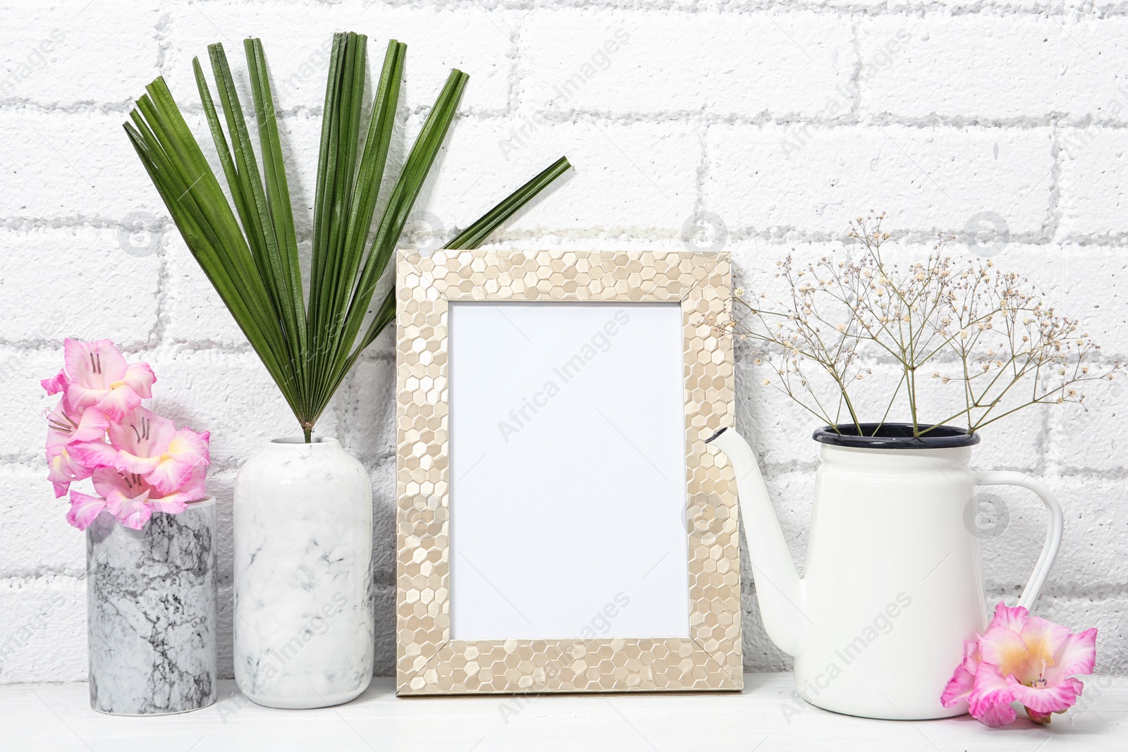 Photo of Blank frame and beautiful plants on table near brick wall. Mock up for design