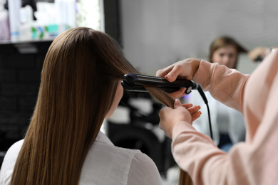 Photo of Hairdresser using straightener to style client's hair in salon
