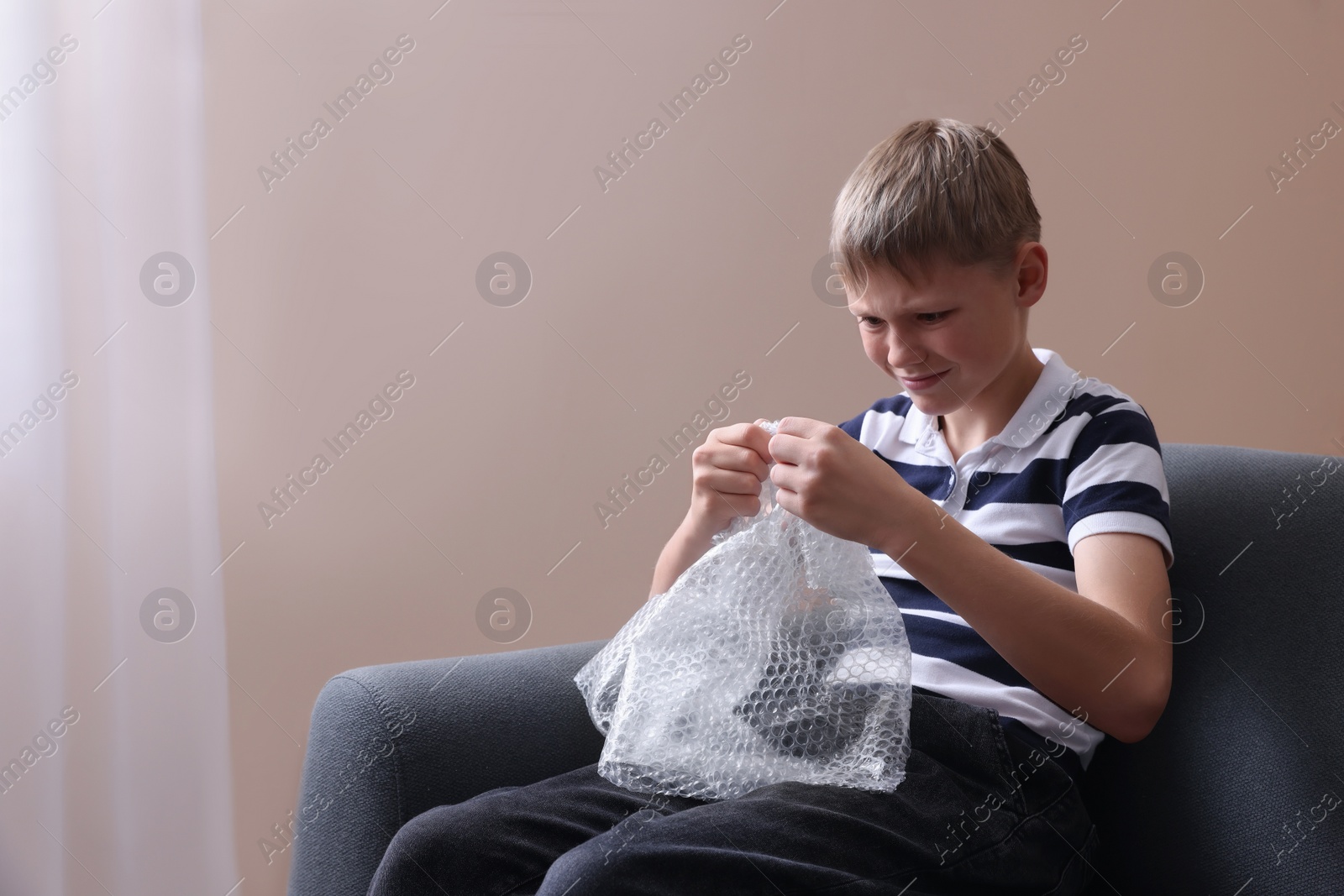 Photo of Emotional boy popping bubble wrap indoors. Stress relief