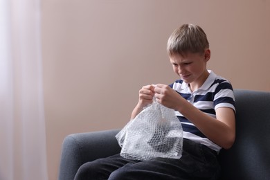 Emotional boy popping bubble wrap indoors. Stress relief