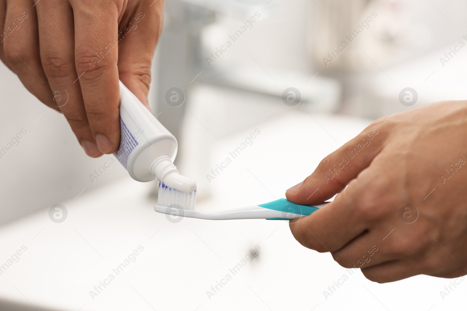 Photo of Man applying toothpaste on brush in bathroom, closeup