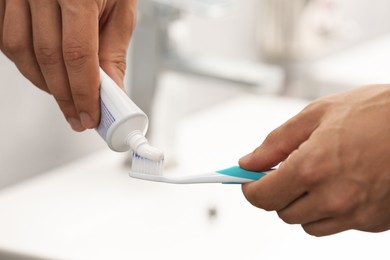 Man applying toothpaste on brush in bathroom, closeup