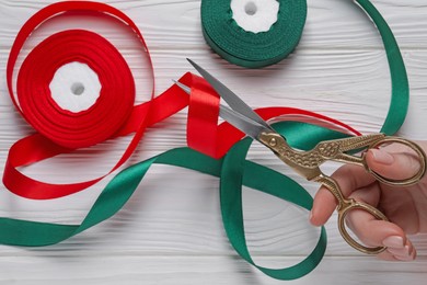 Photo of Woman cutting ribbon with beautiful scissors at white wooden table, closeup