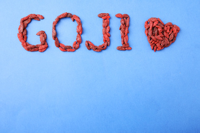 Word GOJI and heart made of dried berries on blue background, flat lay. Space for text