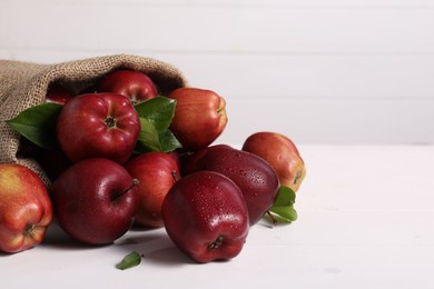 Photo of Ripe red apples and green leaves on white table. Space for text