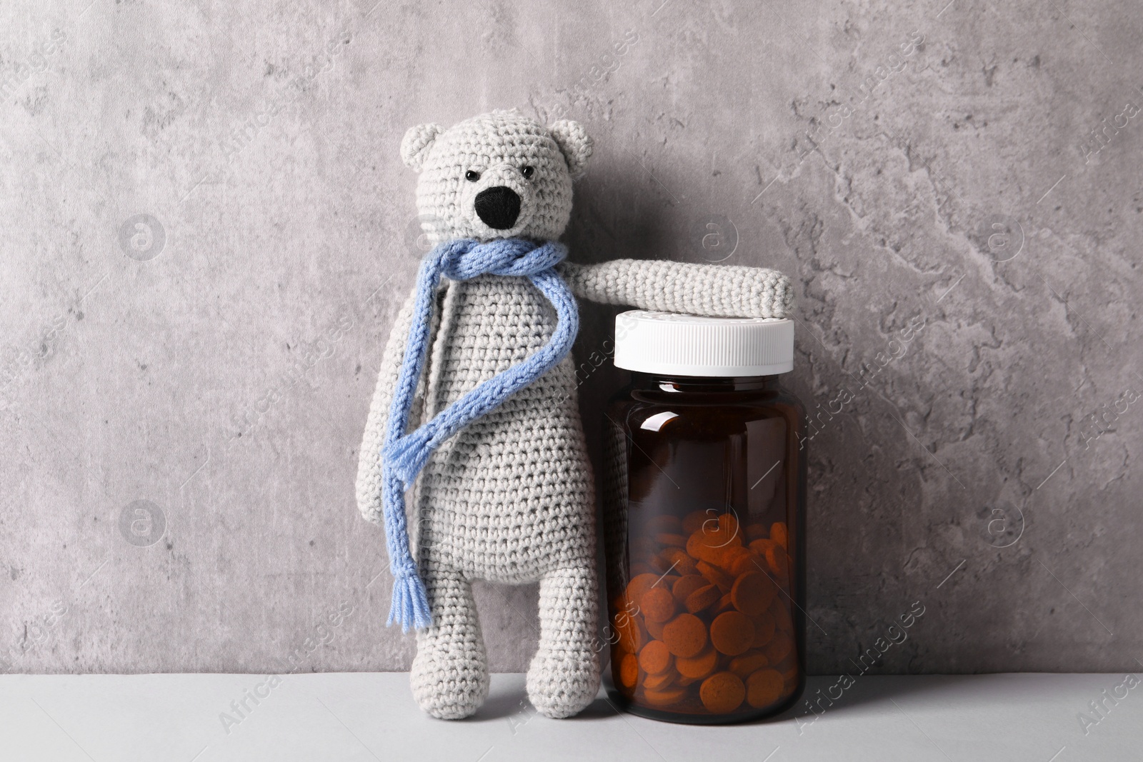 Photo of Toy bear and bottle of pills on light table near grey wall