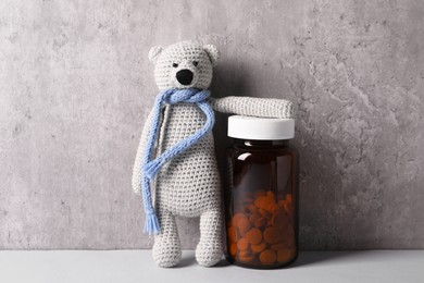 Toy bear and bottle of pills on light table near grey wall