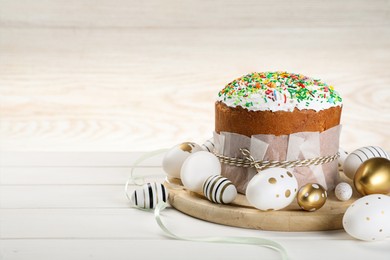 Photo of Traditional Easter cake with sprinkles and painted eggs on white wooden table, space for text
