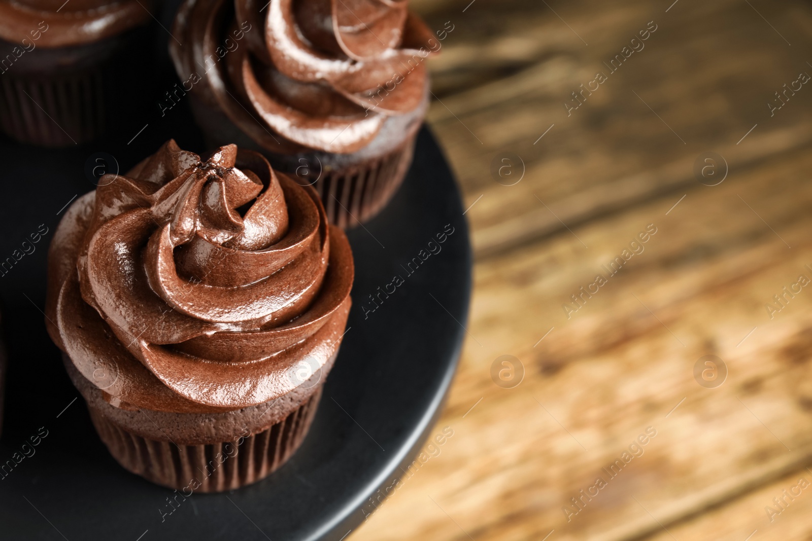 Photo of Dessert stand with delicious chocolate cupcakes on wooden table, closeup. Space for text