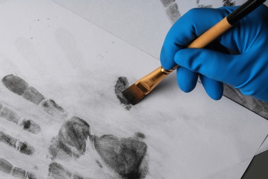 Detective taking fingerprints with brush from paper, closeup. Criminal investigation