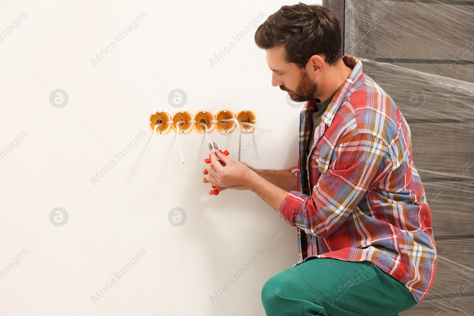 Photo of Professional electrician with pliers fixing wires indoors