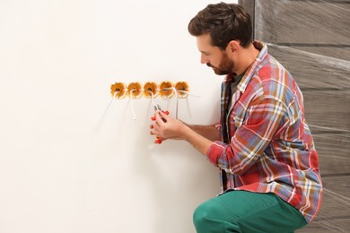 Photo of Professional electrician with pliers fixing wires indoors