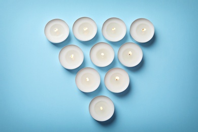 Burning wax candles on color background, top view