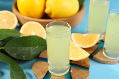Photo of Tasty limoncello liqueur, lemons and green leaves on light blue table, closeup