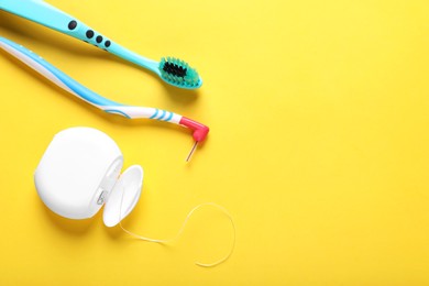 Container with dental floss and toothbrushes on yellow background, flat lay. Space for text