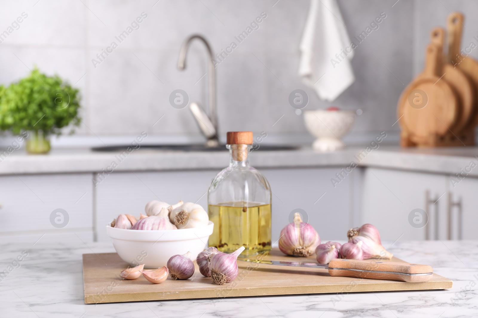 Photo of Fresh raw garlic, knife and oil on white marble table