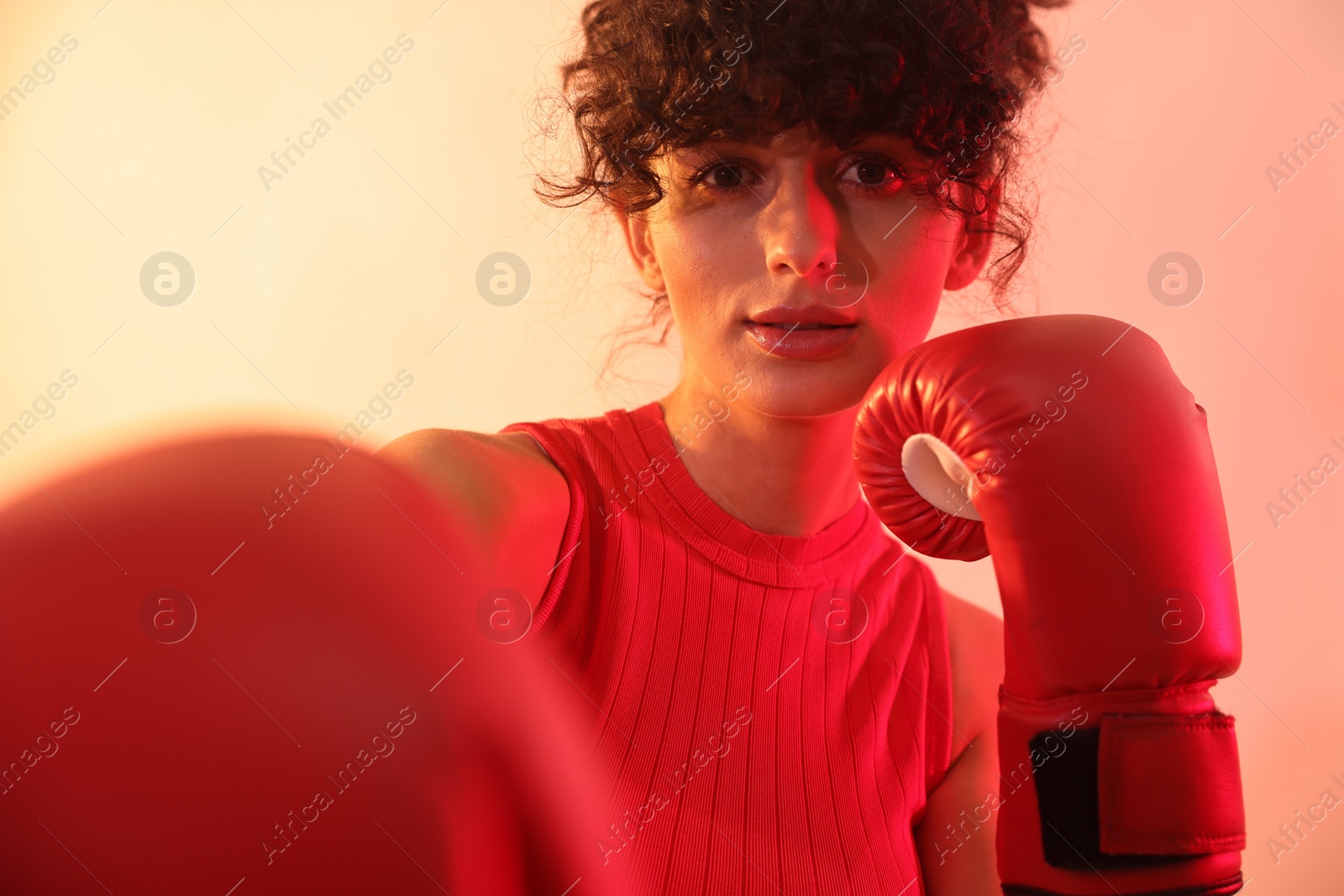 Photo of Beautiful young woman with boxing gloves on color background in neon lights, closeup