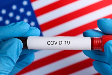 Photo of Scientist holding test tube with blood sample over American flag, closeup. Coronavirus pandemic in USA