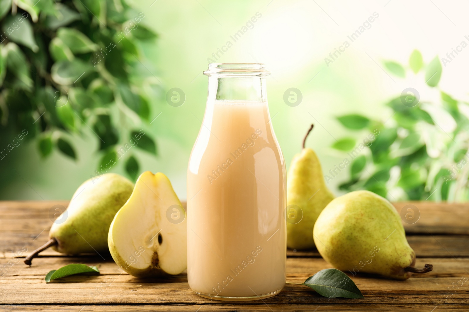 Photo of Fresh pear juice in glass bottle and fruits on wooden table, closeup