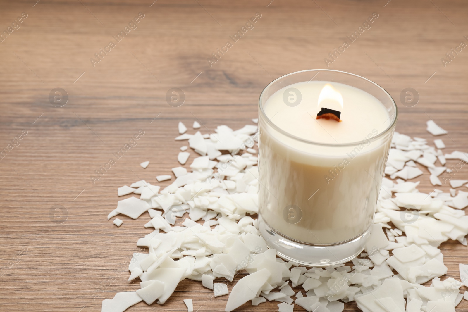 Photo of Burning soy candle and wax flakes on wooden table, space for text