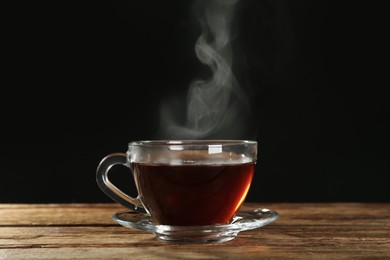 Photo of Cup with steam on wooden table against black background