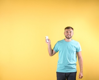 Young man with air conditioner remote on color background, copy space text