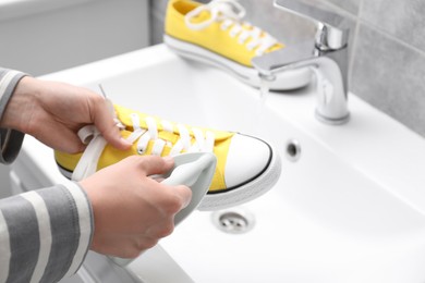 Woman washing stylish sneakers with brush in sink, closeup