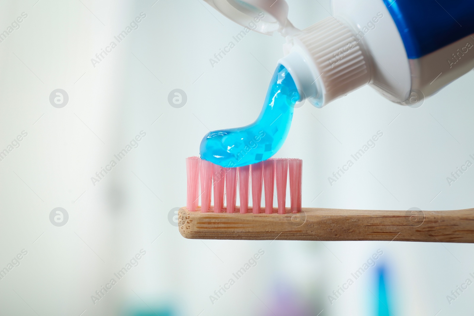 Photo of Applying toothpaste on brush against blurred background, closeup