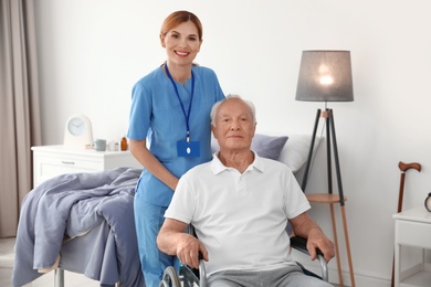 Nurse assisting elderly man in wheelchair indoors