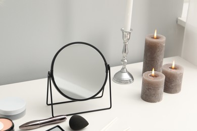 Photo of Dressing table with mirror, cosmetic products and burning candles in makeup room