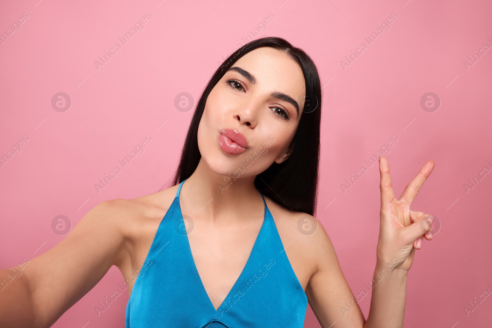 Photo of Beautiful young woman taking selfie while blowing kiss on pink background
