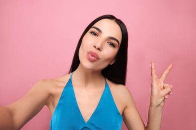 Beautiful young woman taking selfie while blowing kiss on pink background