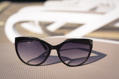 Photo of Stylish sunglasses on grey sunbed outdoors. Beach accessory, closeup