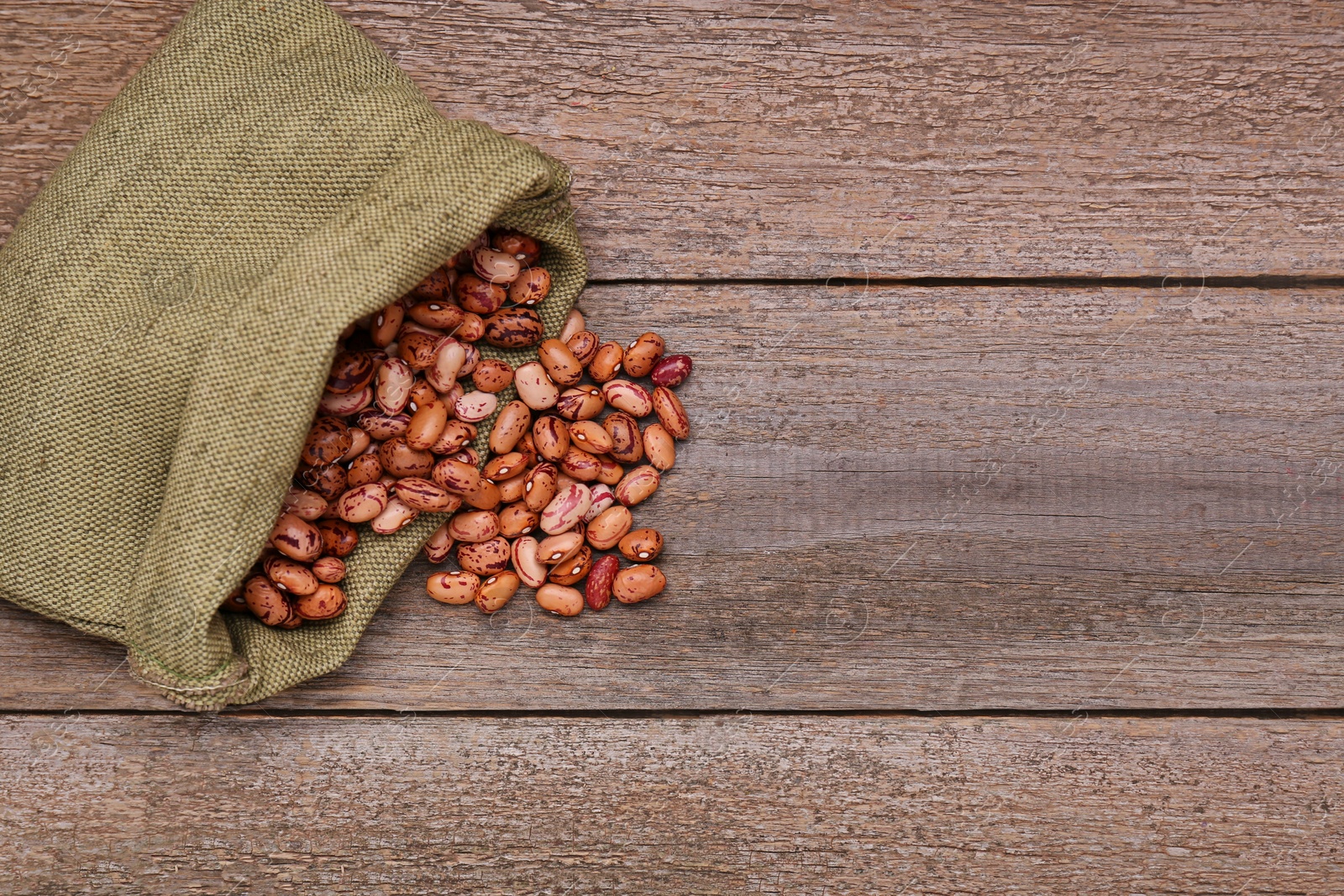 Photo of Overturned sack with dry kidney beans on old wooden table, flat lay. Space for text