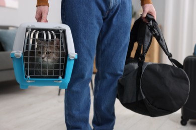 Travel with pet. Man holding carrier with cute cat and bag at home, closeup