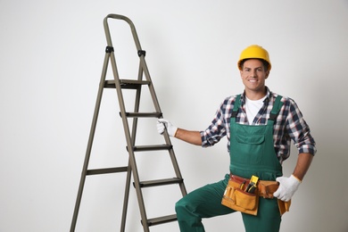 Photo of Professional builder near metal ladder on light background