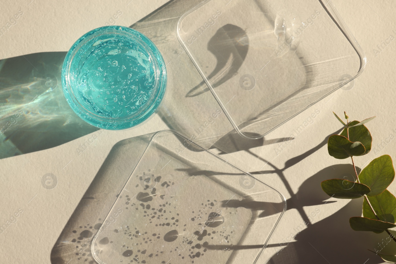 Photo of Jar and samples of transparent cosmetic gel on light table, flat lay