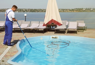 Worker cleaning outdoor swimming pool with underwater vacuum
