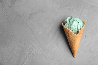 Photo of Delicious spirulina ice cream cone on grey background, top view. Space for text