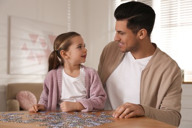 Photo of Man and his little daughter playing with puzzles at home