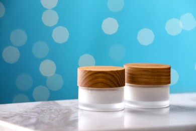 Jars of cream on white table against blurred lights, space for text