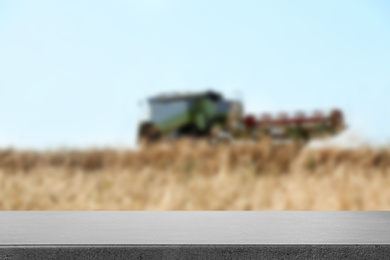 Image of Empty grey stone surface and blurred view of modern combine harvester in wheat field. Space for text