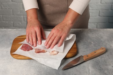 Photo of Woman wiping pieces of meat with paper towels at grey table, closeup