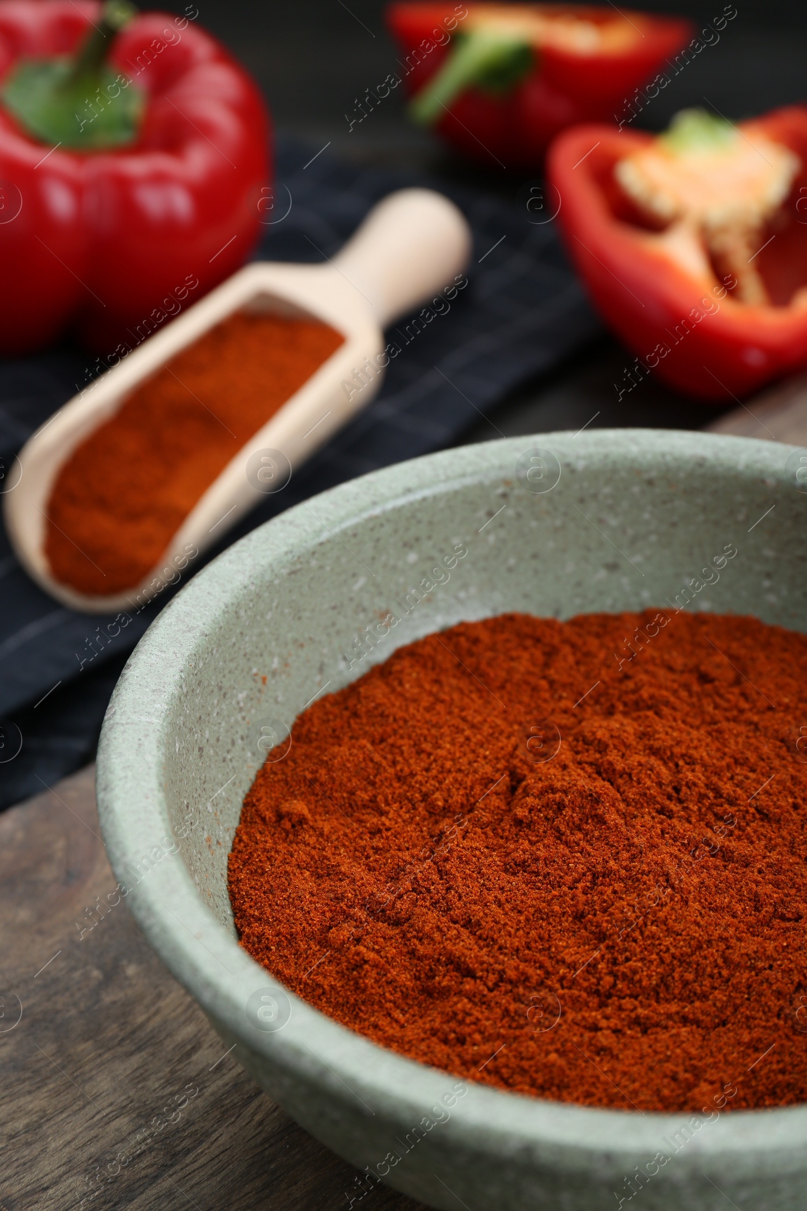 Photo of Bowl of aromatic paprika and fresh peppers on wooden table, closeup