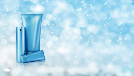 Different cosmetic products on light blue background with blurred snowflakes, space for text. Winter skin care