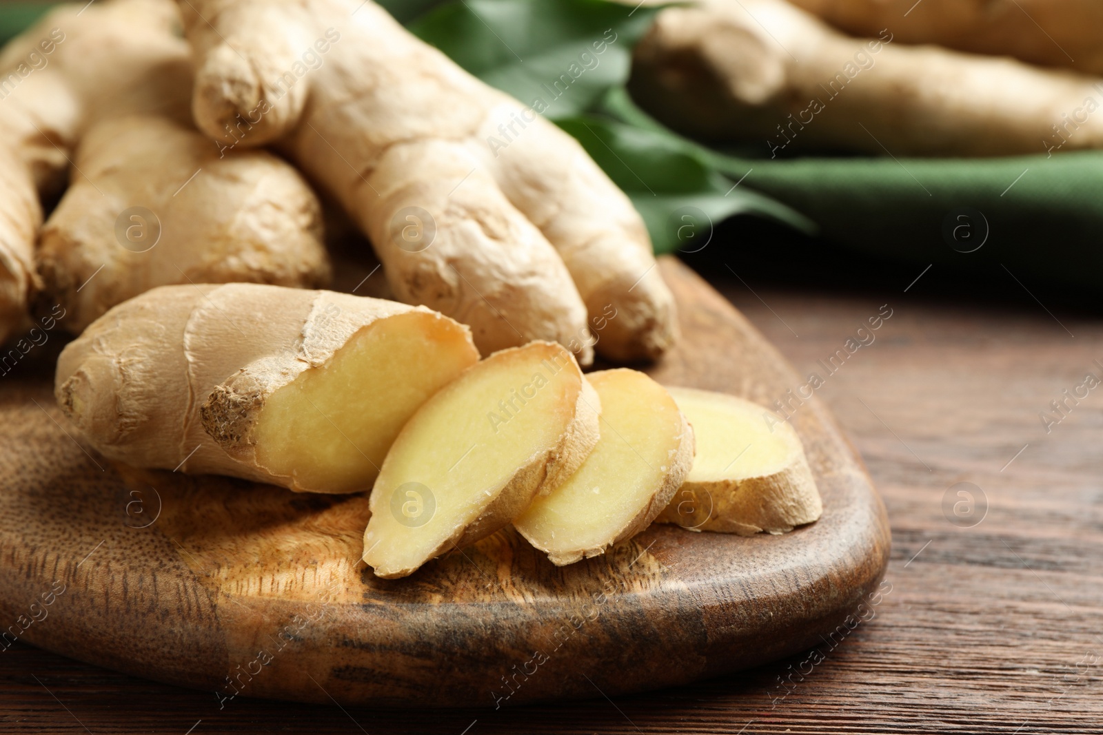 Photo of Cut and whole fresh ginger with leaves on wooden table, closeup