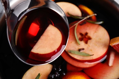 Ladle with delicious mulled wine over cooking pot, closeup