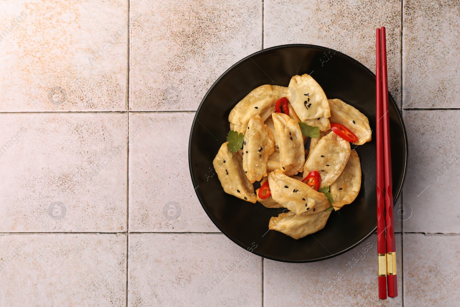 Photo of Delicious gyoza (asian dumplings) and chopsticks on light tiled table, top view. Space for text