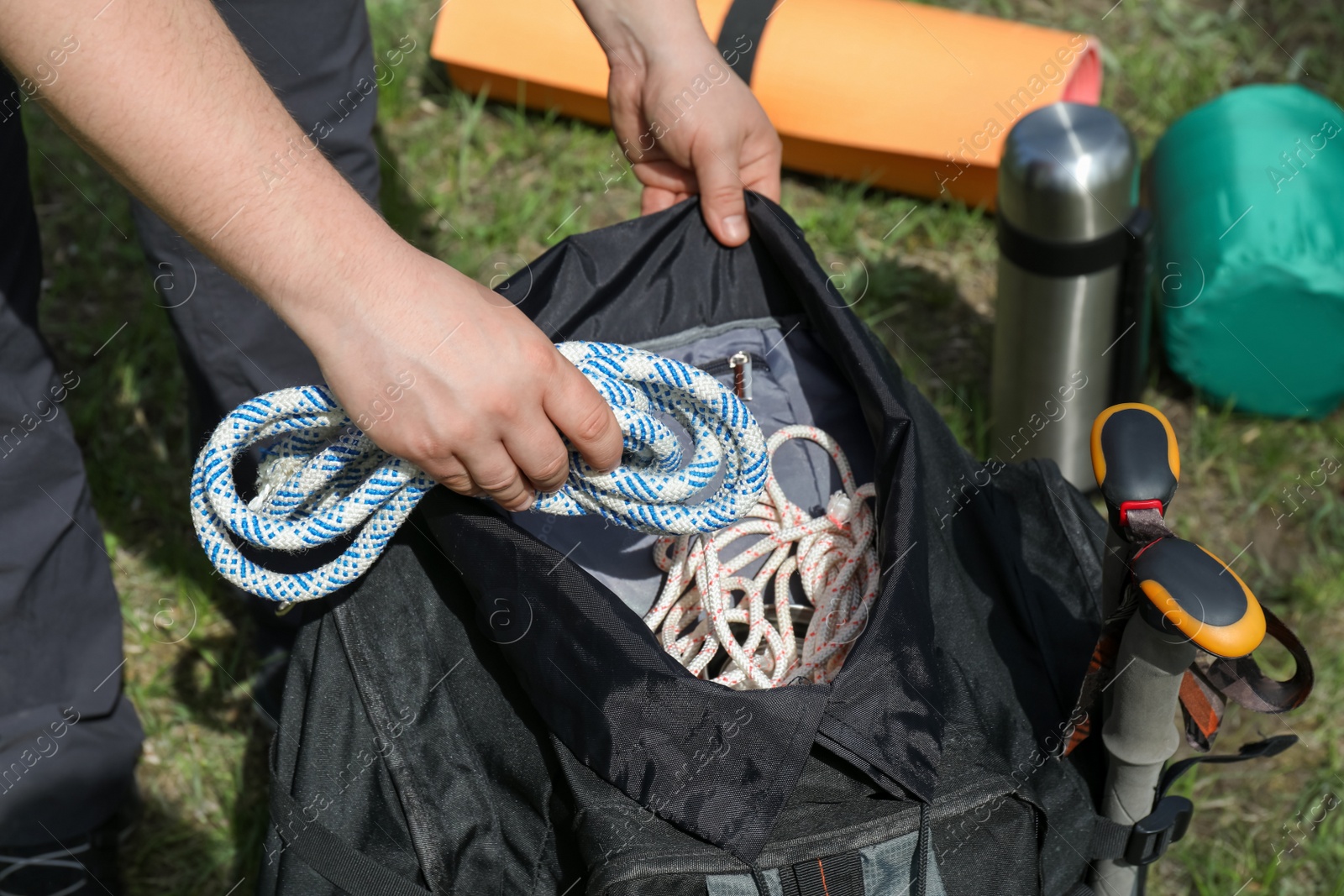 Photo of Hiker putting climbing rope into backpack outdoors, closeup. Mountain tourism